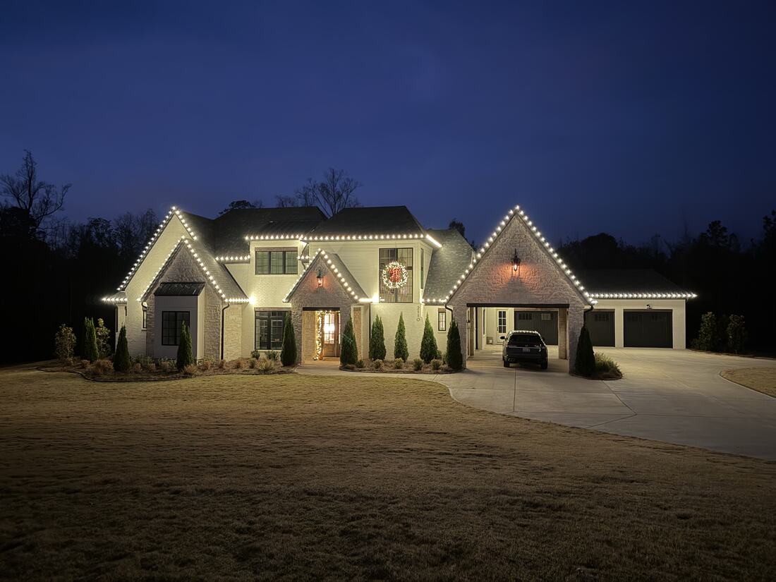 A cream brick home at dusk with roofline lighting running the length of the house and garage